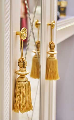 ADH - Detail of white cabinet with mirror and golden tassels hanging on knobs